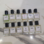 Ten small rectangular glass perfume bottles with black caps arranged in two rows on a light marble surface. The bottles contain clear or lightly tinted liquid and have white labels with black text, including scents such as Energy, Boss, Decent Man, Legend, Pineapple, Alpha, Ice Cube, Beast, Rebel, and Alone.2